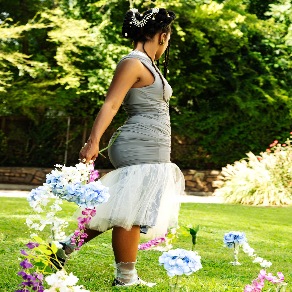 Woman in a gray dress with a white skirt walking through a garden with flowers. Sirens in Blue – Sheer Statement Legwear for Women